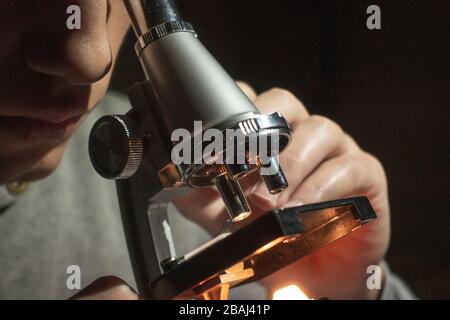 Young scientist doing research looking through his microscope late at night at his home Stock Photo