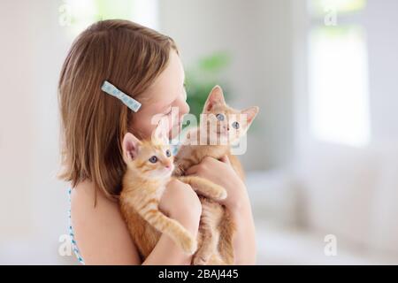 Child holding baby cat. Kids and pets. Little girl hugging cute little kitten at home. Domestic animal in family with kids. Children with pet animals. Stock Photo