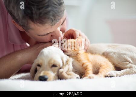 Cat and dog sleeping together next to a man. Kitten and puppy taking nap with owner. Home pets. Animal care. Love and friendship. Domestic animals. Stock Photo