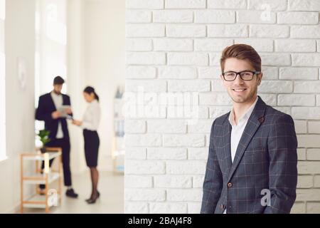Smiling positive businessman in casual attire standing in a white office on a white wall. Stock Photo