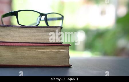 Reading glasses on top of stack of books. Garden or green nature background. Stock Photo