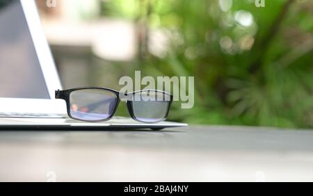 Spectacles on top of computer laptop with home and green nature background. Copy space. Work remotely or from home concept. Stock Photo