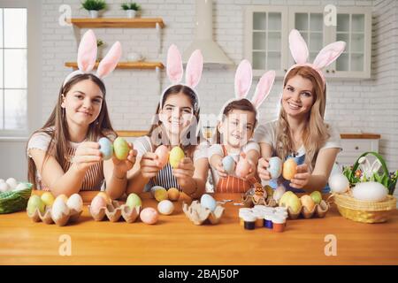 Happy easter. Mother and daughters with rabbit ears decorate Easter eggs at a table in kitchen. Stock Photo