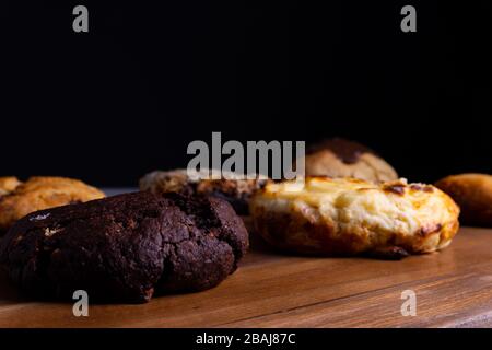 Different cookie cakes laying on a wooden board in front of a black background Stock Photo