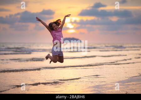Child playing on ocean beach. Kid jumping in the waves at sunset. Sea vacation for family with kids. Little girl running on  exotic island during summ