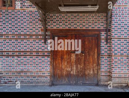 Grunge wooden decorated arched entrance gate with wooden canopy above on wall with black and red bricks with white seam Stock Photo