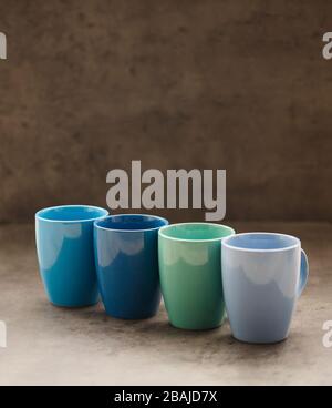 four tea mugs of different colors on a gray background Stock Photo