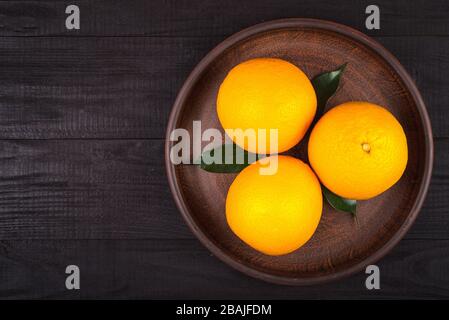 three oranges with green leaves lie in a brown plate on a brown table. background Stock Photo
