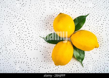 three lemons with green leaves are dotted on a white surface. background. juicy citrus fruits Stock Photo