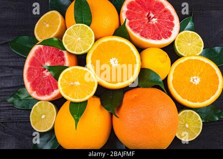 fruits, half grapefruits, lemons, oranges, limes with green leaves lie on a brown wooden table. background. view from above Stock Photo