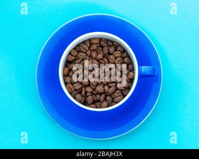 Cup full of coffee beans isolated on blue background Stock Photo