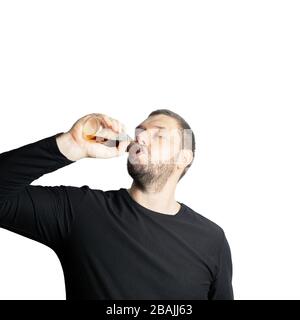 Dark-haired bearded man in dark clothes drinks a dark drink from bottle closing his eyes in pleasure Stock Photo