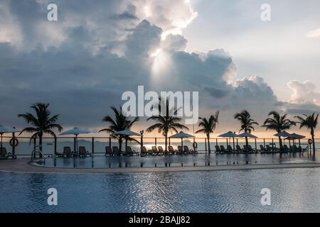 Swimming pool, palm trees around, reflection of palm trees in the pool, dawn with a beautiful cloudy sky. An empty area with many sunbeds, the sun pas Stock Photo