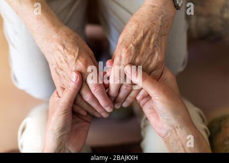 Nurse consoling her elderly patient by holding her hands Stock Photo