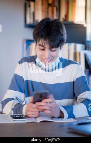 A college student wearing a mask and taking time out from his studies to message on his mobile phone Stock Photo