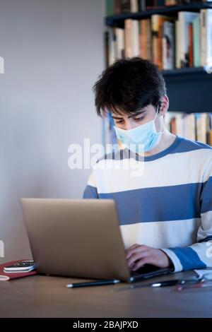 A teenager wearing a protective mask studying on their lap top at home Stock Photo