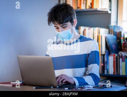 A teenager wearing a protective mask studying on their lap top at home Stock Photo