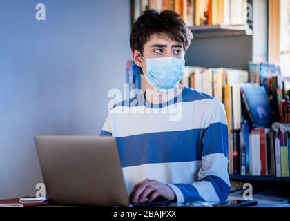 A teenager wearing a protective mask studying on their lap top at home Stock Photo