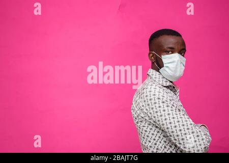 a young african doctor isolated over pink background wearing face mask to prevent himself from the outbreak, disease and flu. Stock Photo