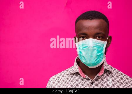 a young african doctor isolated over pink background wearing face mask to prevent himself from the outbreak, disease and flu. Stock Photo