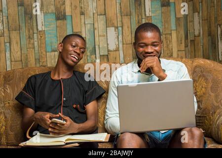 two african young businessmen seriously working with their mobile phone and laptop feeling about what they saw on their device Stock Photo