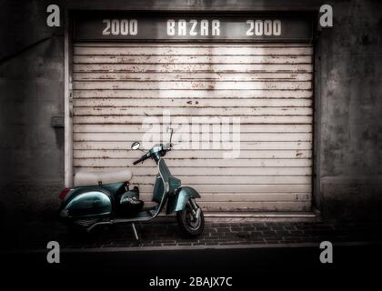 A classic italian scooter parked on the street in front of a rusty metal shutter of an old shop front, Numana, Italy Stock Photo