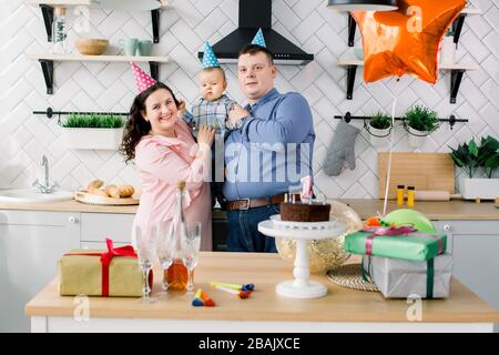 Young family celebrating first birthday of their little baby boy with a cake, present boxes, and air balloons. Birthday party concept, family and Stock Photo