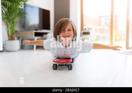 Boy with arms open lying on skateboard at home Stock Photo