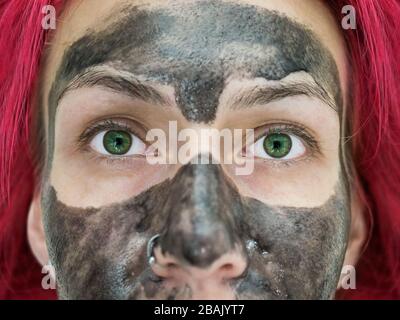 Close-up photo of a fragment of the face of a girl with bright green eyes,  red hair and black peel off mask on her face Stock Photo - Alamy