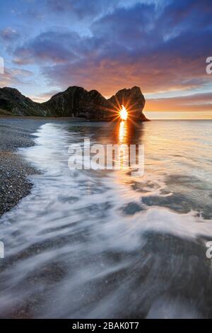 Sun shining through Durdle Door at sunrise, Jurassic Coast, Dorset, England, UK Stock Photo