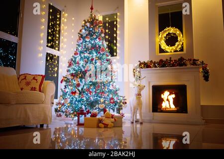 Christmas tree in decorated living room. Family home winter season decoration. Present and gift boxes on Xmas eve. Fireplace with garlands, ornaments Stock Photo