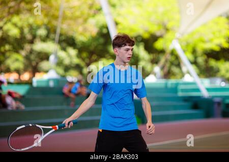 Young man playing tennis on open court. Teenager with racquet at competition match. Healthy outdoor sport for high school or college kids. Student exe Stock Photo