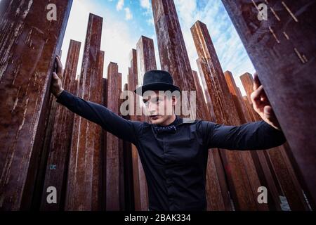 Portrait of a young male athlete in elegant, stylish outfit among raw, rusty iron poles Stock Photo