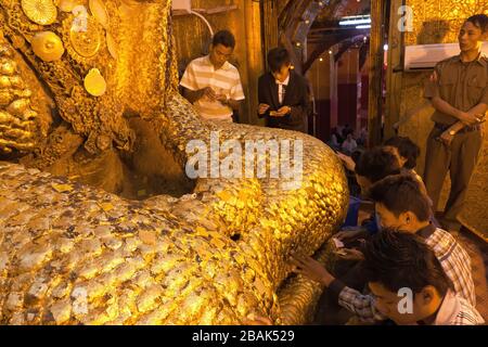 Male devotees attaching golden leaves to the Mahamuni Buddha statue, Mandalay, Myanmar Stock Photo