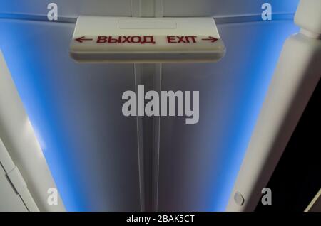 Luminous sign "exit" in Russian and English inside the aircraft high above the head on a blue background with illumination Stock Photo