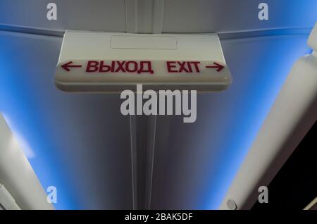 Information luminous sign 'exit' in Russian and English in the plane on the background of the ceiling with a blue light Stock Photo