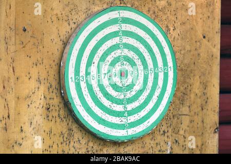 Green and white dartboard on a wooden wall photographed in Finnish summer cottage. Playing darts is a fun way to spend summer holiday. Relaxing! Stock Photo