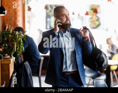 Young bearded businessman walks into a stylish loft office talking on the phone. Stock Photo
