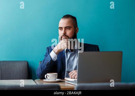 Businessman bearded man in a suit works behind the laptop sitting in a comfortable office coworking. Stock Photo