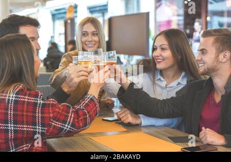 Group of people hanging with each other in a bar and cheering with beer- Friends enjoying fiendship time and talking with each other happy- Lifestyle Stock Photo