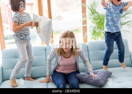 Mother with headache and children jumping on sofa Stock Photo