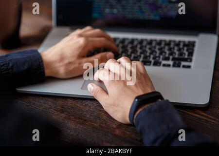 a male programmer in a black shirt is working at a laptop, close-up of the program code and developer's hands on a laptop. modern young programmer sit Stock Photo