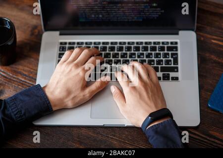 a male programmer in a black shirt is working at a laptop, close-up of the program code and developer's hands on a laptop. modern young programmer sit Stock Photo
