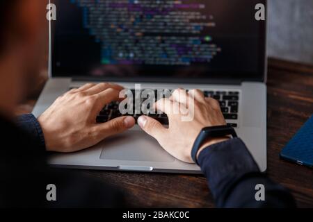 a male programmer in a black shirt is working at a laptop, close-up of the program code and developer's hands on a laptop. modern young programmer sit Stock Photo