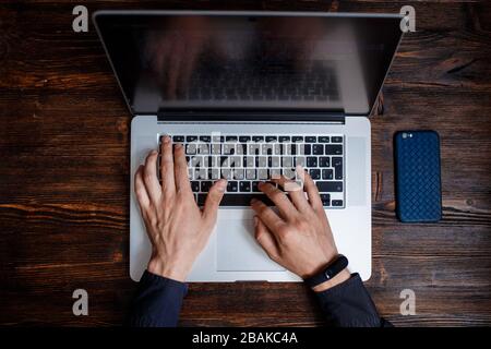 a male programmer in a black shirt is working at a laptop, close-up of the program code and developer's hands on a laptop. modern young programmer sit Stock Photo