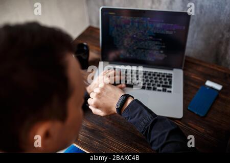 a male programmer in a black shirt is working at a laptop, close-up of the program code and developer's hands on a laptop. modern young programmer sit Stock Photo