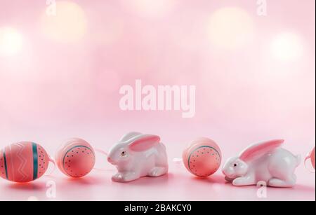 Colored decorated eggs and porcelain bunnies on pink background. Easter concept, card with free copy space. Stock Photo