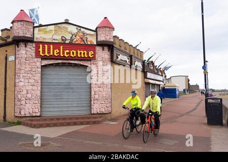 Portobello, Scotland, UK. 28 March, 2020. On the first weekend of the coronavirus lockdown the public were outdoors exercising and maintaining social distancing along Portobello beachfront promenade. Pictured; cyclists on promenade and closed amusement arcade. Iain Masterton/Alamy Live News Stock Photo