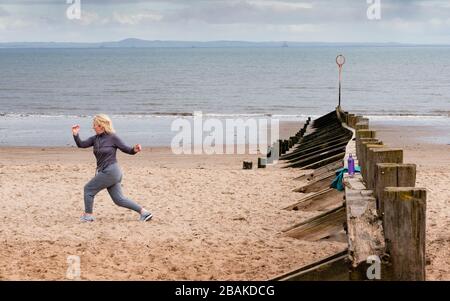 Portobello, Scotland, UK. 28 March, 2020. On the first weekend of the coronavirus lockdown the public were outdoors exercising and maintaining social distancing along Portobello beachfront promenade. Pictured; Annabel Meikle from Portobello working out on her special covid-19  solo training program set by her personal trainer. Iain Masterton/Alamy Live News Stock Photo