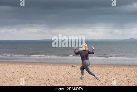 Portobello, Scotland, UK. 28 March, 2020. On the first weekend of the coronavirus lockdown the public were outdoors exercising and maintaining social distancing along Portobello beachfront promenade. Pictured; Annabel Meikle from Portobello working out on her special covid-19  solo training program set by her personal trainer. Iain Masterton/Alamy Live News Stock Photo